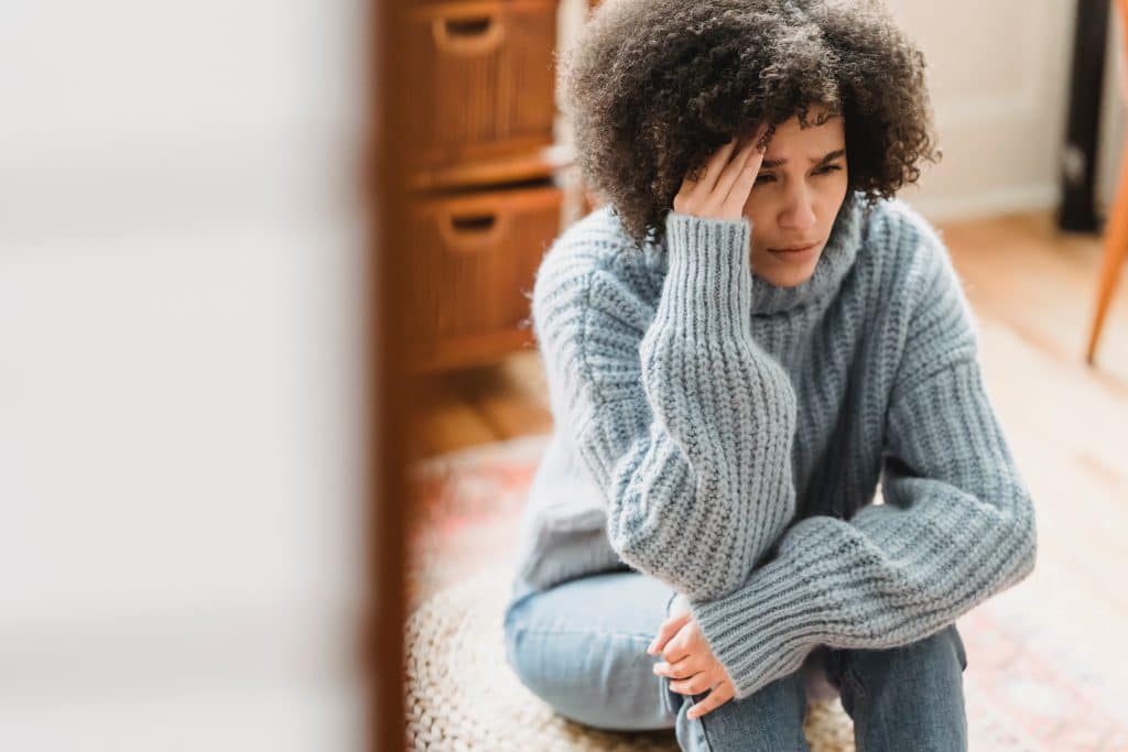 Woman with gray sweater sitting on the floor worried about fibromyalgia pain - Specialists in NY